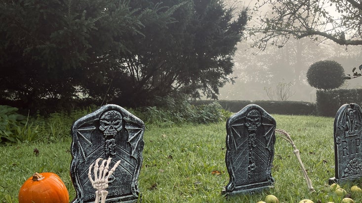 An image of Halloween decorations amongst the mist at Trerice, including grave stones and fake skeleton bones.